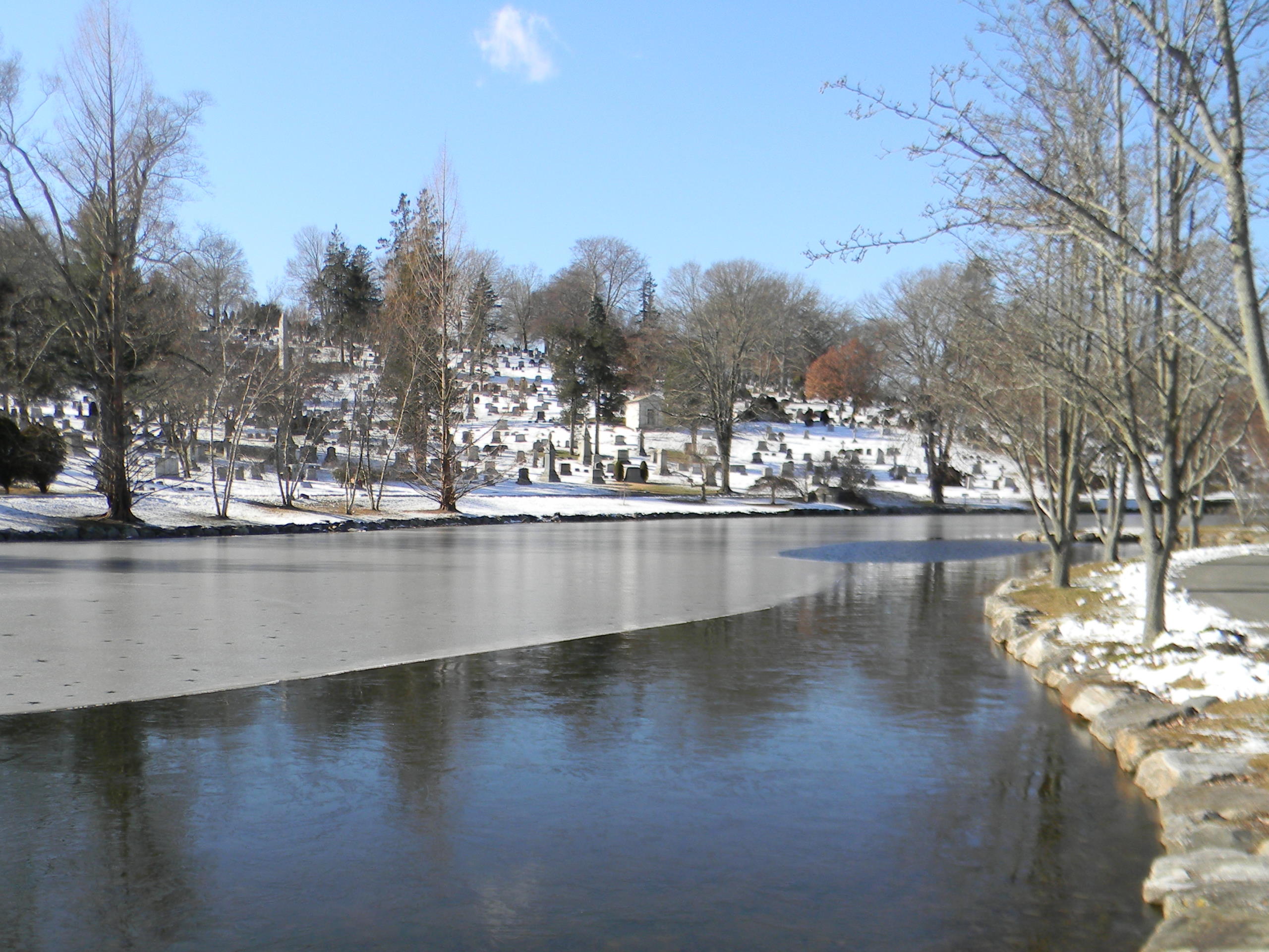 A half-frozen lake and the cemetery on the hill covered in snow.